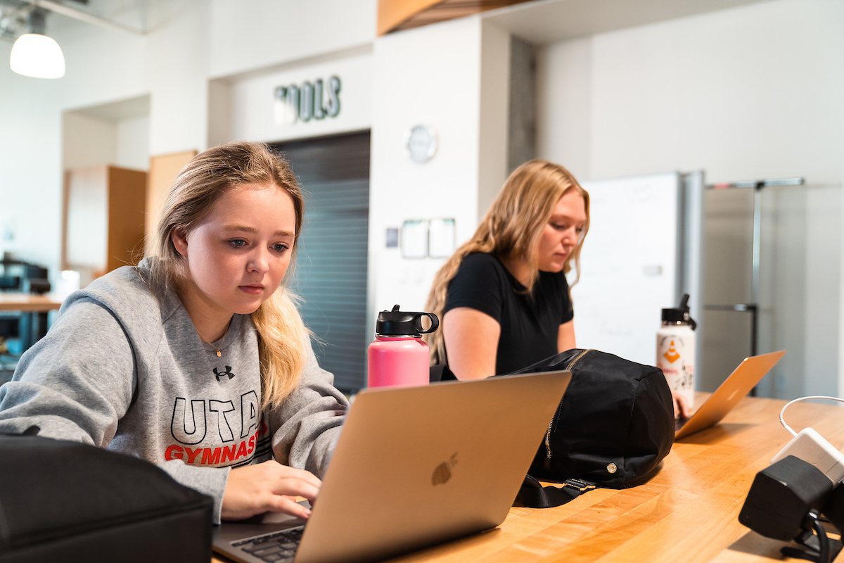 Two University of Utah students seated and focused on their laptops.
