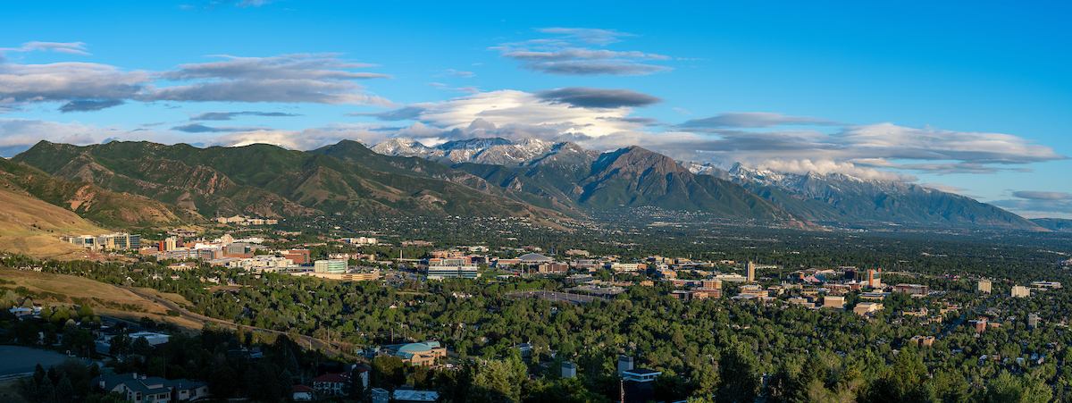 Decorative landscape photo of the university of utah campus with green trees, mountains in the background and blue sky with clouds. Decorative landscape photo of the university of utah campus with green trees, mountains in the background and blue sky with clouds.